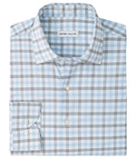 A neatly folded Lucas Performance Twill Sport Shirt by Peter Millar, featuring long sleeves and a button-down design with a light blue, grey, and white plaid pattern. Crafted from performance fabric, this shirt seamlessly blends style and comfort for any occasion.