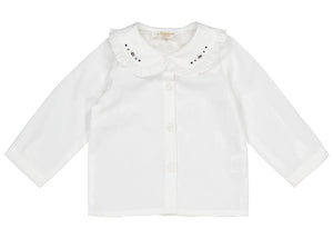 The Kidiwi Baby Girls' Hélena Blouse features off-white plumetis fabric, long sleeves, a ruffled Peter Pan collar with navy embroidery, and a button-down front with delicate decorative details.