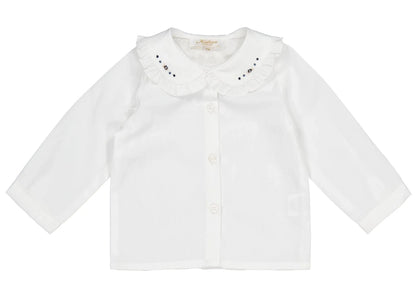 The Kidiwi Baby Girls' Hélena Blouse features off-white plumetis fabric, long sleeves, a ruffled Peter Pan collar with navy embroidery, and a button-down front with delicate decorative details.