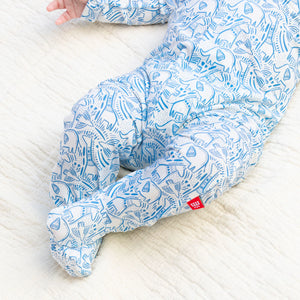 A baby wearing Magnetic Me's Baby' Heards of Feather Modal Footie with feet lies on a cream-colored textured blanket.