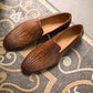 A Herrera Woven Loafer by Magnanni, made of rich brown leather, elegantly rests on an ornate mosaic tiled floor, reflecting Línea Flex's artistry.