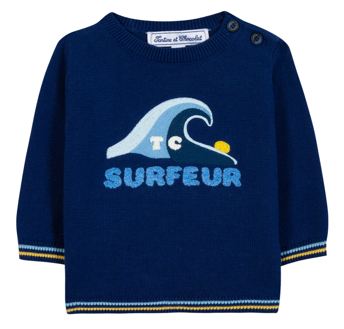 The Tartine et Chocolat Baby Boys’ and Toddler Knitted Sweater is a navy blue long-sleeve piece for kids, made from 100% cotton and featuring a wave graphic, “SURFEUR” text, and two buttons on the shoulder.
