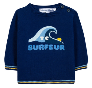 The Tartine et Chocolat Baby Boys’ and Toddler Knitted Sweater is a navy blue long-sleeve piece for kids, made from 100% cotton and featuring a wave graphic, “SURFEUR” text, and two buttons on the shoulder.