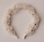 The Noralee Gathered Headband features white tulle adorned with gold and black star sequins, perfect for special occasions and shown on a light textured surface.