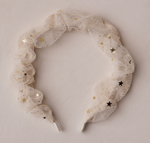 The Noralee Gathered Headband features white tulle adorned with gold and black star sequins, perfect for special occasions and shown on a light textured surface.