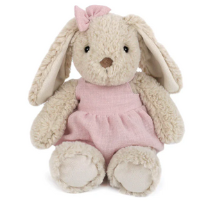 Bettie Bunny - Pink by Mon Ami is a beige plush bunny with floppy ears, dressed in a pink dress and matching bow, sitting facing forward against a white background. This soft stuffed animal is perfect for cuddles and display.