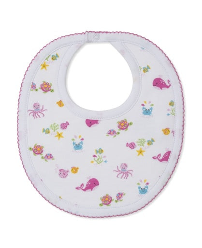 The Kissy Kissy Ocean Antics Printed Bib features a white base with pink trim, made from the softest cotton for ultimate comfort, and is decorated with colorful prints of sea creatures such as whales, octopuses, turtles, fish, and starfish.