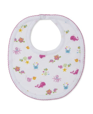 The Kissy Kissy Ocean Antics Printed Bib features a white base with pink trim, made from the softest cotton for ultimate comfort, and is decorated with colorful prints of sea creatures such as whales, octopuses, turtles, fish, and starfish.