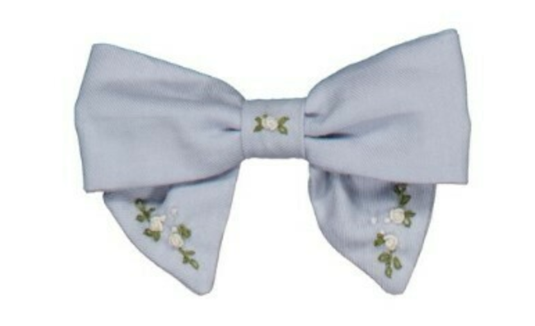 The Kidiwi Bonnie Embroidered Hair Clip is light blue with a large bow, detailed with small white floral embroidery and green leaves on the tails, shown on a plain white background.