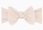 The Baby Bling Classic Knot Headband by Baby Bling is a sizeable bow in a soft pink fabric, exhibiting high-quality material and a meticulously crafted knotted center set against a simple white background.