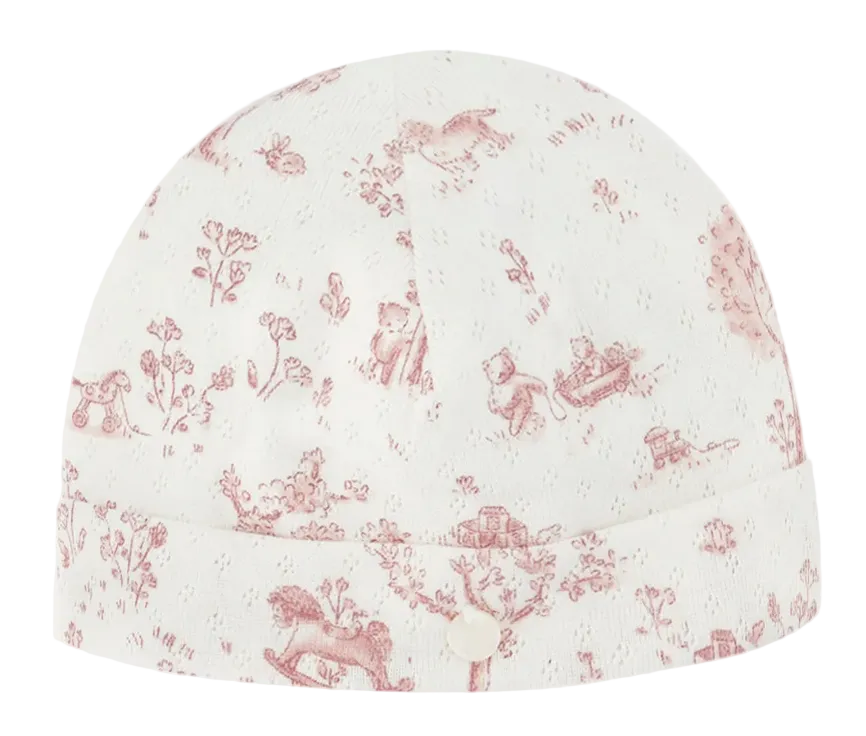 The Baby Fantasy Garden Cotton Beanie by Tartine et Chocolat is a white baby hat adorned with a delightful fantasy garden print in pink, featuring charming illustrations of toys, animals, and plants, and accented with a small fabric button on the front.