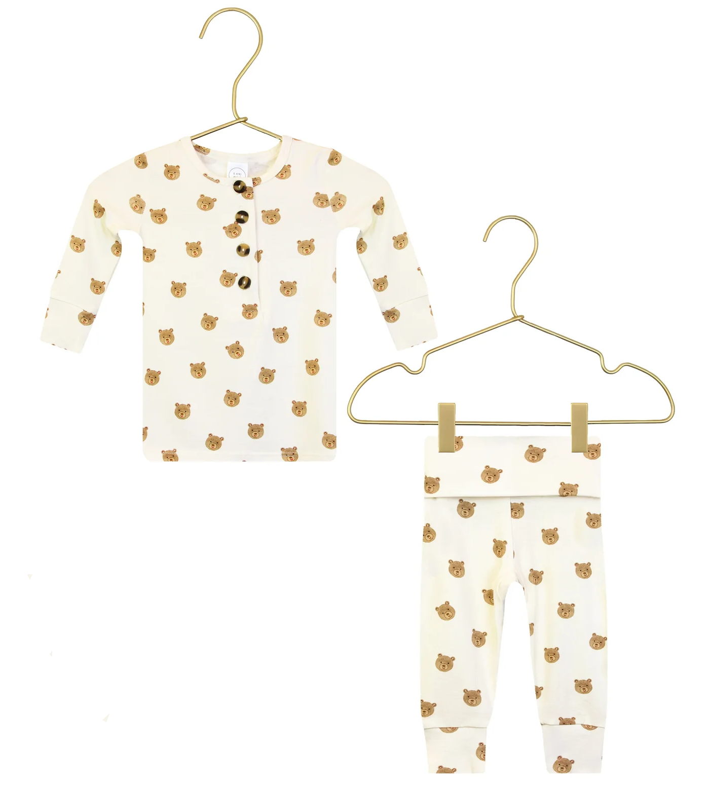 The Lou Lou & Company Baby Boys’ and Boys’ Teddy Top & Bottoms set features a two-piece cream-colored outfit, including a long-sleeve, buttoned shirt and matching pants adorned with an adorable brown bear face print. The pants are designed with a comfy fold-over waistband for extra flexibility. Displayed on gold hangers against a white background.