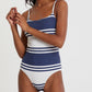 A woman wears the Lemlem Elene One Piece, a classic blue and white striped swimsuit with adjustable spaghetti straps, standing against a plain white background.