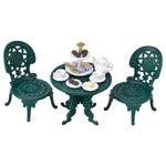 The Calico Critters Tea and Treats Set features two ornate green chairs and a matching garden table, charmingly arranged with tea party accessories like a white teapot, teacups, plates, and a tray of assorted pastries and sweets.
