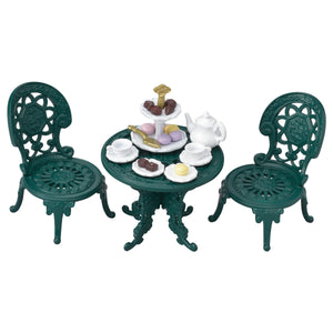 The Calico Critters Tea and Treats Set features two ornate green chairs and a matching garden table, charmingly arranged with tea party accessories like a white teapot, teacups, plates, and a tray of assorted pastries and sweets.