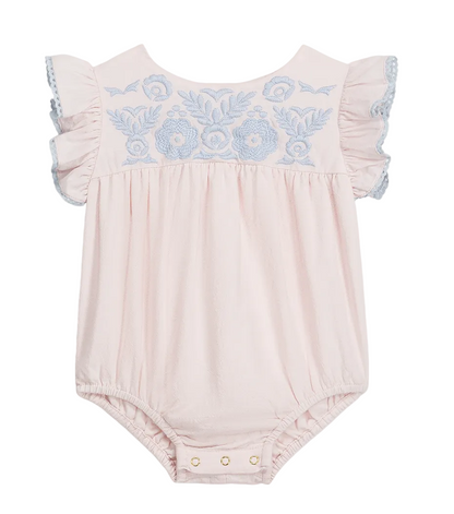 The Louise Misha Baby Girls’ Nusha Romper is crafted from soft cotton gauze in a light pink hue, featuring short ruffled sleeves, an embroidered yoke with delicate blue floral detailing on the chest, and convenient snap closures at the bottom.