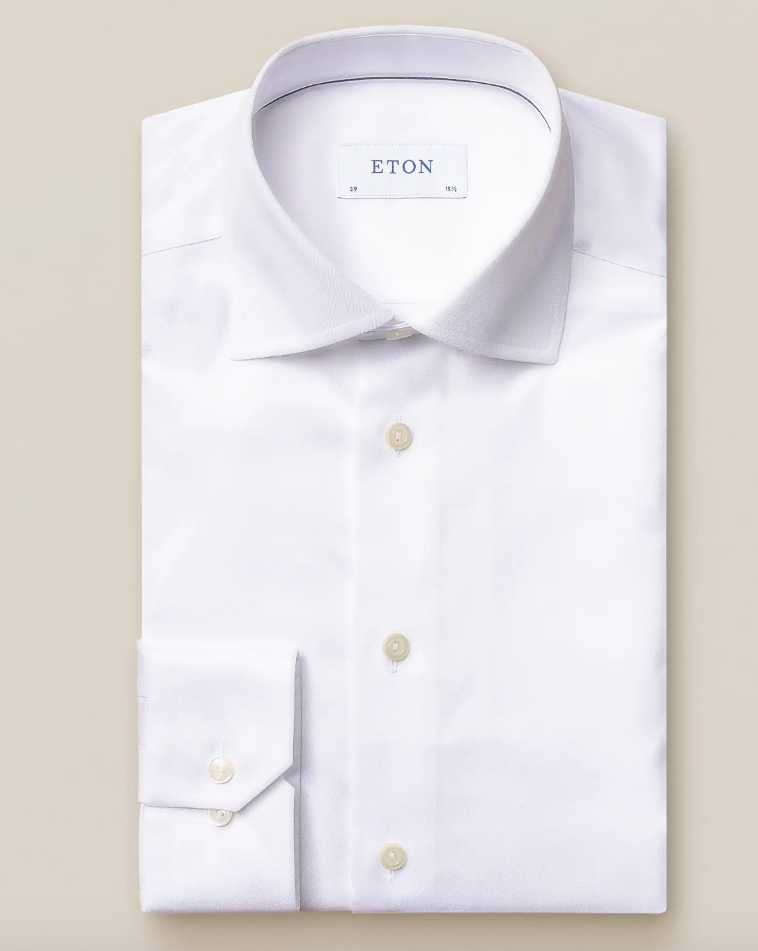 The Eton White Signature Twill Shirt, Slim Fit, features a classic collar and buttoned cuffs with the brand label inside, offering a versatile and impeccable look. Elegantly displayed on a beige background.