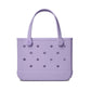 The Bitty Bogg® Bag by Bogg Bags is a compact lavender tote with round holes and two handles, featuring “bogg” embossed on the bottom right corner. This washable bag is perfect for everyday use.