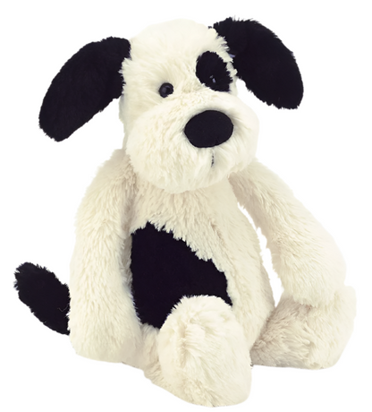 The Jellycat Bashful Black & White Puppy, Medium, is a plush toy with soft white fur, black ears, a black patch over one eye, and a black spot on its side, shown in an upright sitting position.