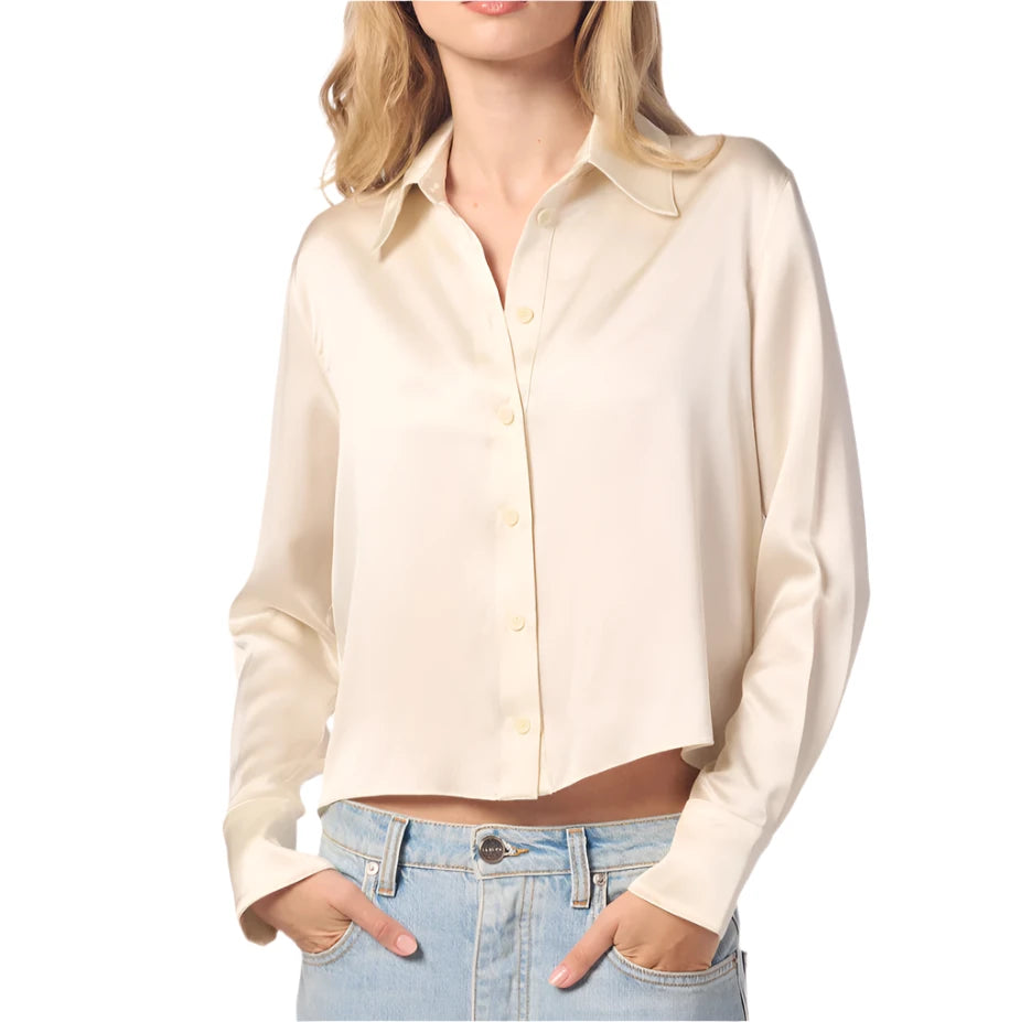 Dressed in the Sablyn Yves Silk Button Down Top, a cream-colored long-sleeve blouse, and pairing it with light blue jeans, a person exudes a sophisticated silhouette while posing with hands in pockets.