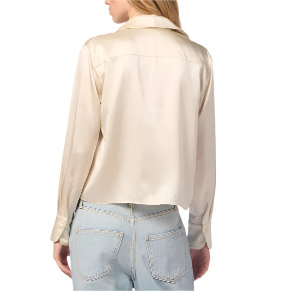 A person wearing the Sablyn Yves Silk Button Down Top in cream, showcasing a sophisticated silhouette with long sleeves and a collar, is paired with light blue jeans and shown from the back.