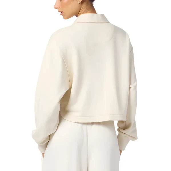 A person is seen from the back, wearing the Sablyn Holden Henley Sweatshirt, a cream-colored long-sleeve top with a subtle curved hem, paired with matching pants to create an effortlessly chic look.