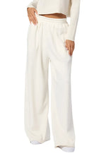 A person wearing Sablyn's Hayes Sweatpant, which features high-waisted, wide-leg front pleats in white, and a cropped long-sleeve top, with one hand resting on the hip.