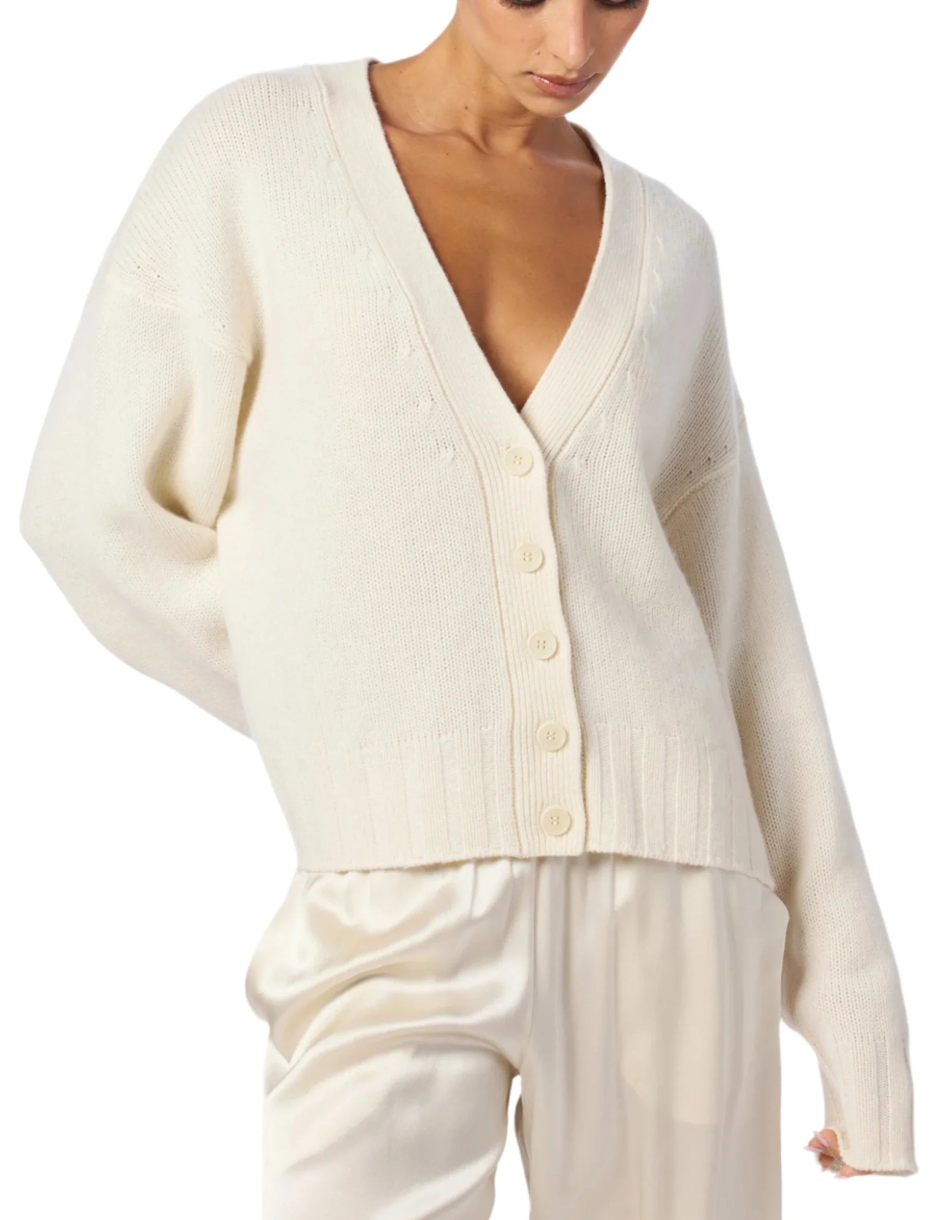 A person wearing the Sablyn Tisch Relaxed Cardigan, a versatile off-white cashmere piece featuring a deep V-neck and buttons, paired with matching pants.