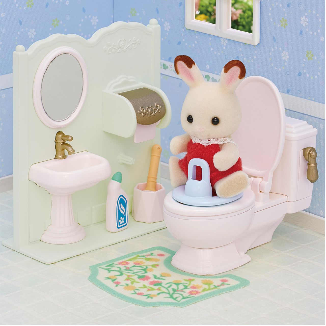 A Calico Critters Toilet Seat is featured in a miniature bathroom scene with a toy rabbit in a red dress, surrounded by a sink, mirror, cleaning accessories, and a patterned rug.