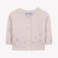 The Baby Girls’ and Girls’ Emeraude Embroidery Floral Cardigan by Tartine et Chocolat is a light pink knit cardigan made from soft wool, adorned with white buttons and delicate blue floral embroidery along the bottom edge and sleeves, displayed against a plain white background.