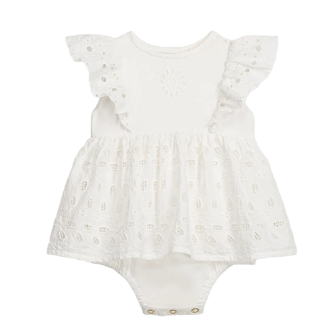 The Louise Misha Baby Girls’ Lenali Romper is a white cotton dress-style romper adorned with delicate eyelet embroidery on the ruffled sleeves, a gathered skirt, and convenient snap buttons at the bottom.