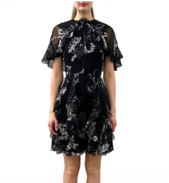 A woman wears the Jason Wu Collection SS Printed Chiffon Dress, a short black dress with white floral prints, ruffled short sleeves, and a high neckline, standing against a plain white background.