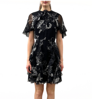 A woman wears the Jason Wu Collection SS Printed Chiffon Dress, a short black dress with white floral prints, ruffled short sleeves, and a high neckline, standing against a plain white background.