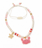 The Crab Red Necklace by Lillies & Roses features pink, white, and gold beads accented with a playful pink crab charm and a gold starfish charm. This whimsical piece captures the signature style of the Crab Red Necklace while adding beachy flair, shown here against a crisp white background.