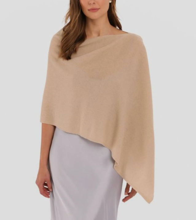 A woman models the Alashan Cashmere Dress Topper Poncho in light beige, layered over a light lavender satin dress—demonstrating this versatile wardrobe essential against a plain background.