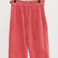 The Girls’ July Pants by Bonpoint are crafted from organic cotton corduroy in coral pink, featuring a wide-leg design and an elastic waistband, shown on a light-colored hanger against a white background.