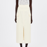 The individual is dressed in a white patterned top with Ulla Johnson's Rhodes Skirt, a long cream cotton Tencel piece that features large pockets and a front slit.