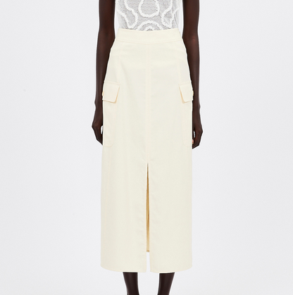 The individual is dressed in a white patterned top with Ulla Johnson's Rhodes Skirt, a long cream cotton Tencel piece that features large pockets and a front slit.
