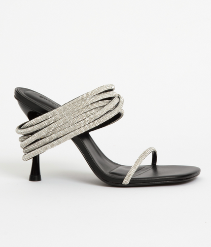 The Simkhai Infinity Crystal Strap Siren Sandal features a black high heel, thin toe strap, and multiple coiled crystal-embellished straps, perfect for evening wear and shown against a plain white background.