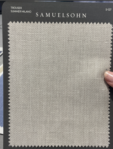 A swatch of light beige textured fabric labeled "Samuelsohn Slim Fit Flat Front Wool Pants," ideal for slim dress pants, is held by a hand on the right edge.