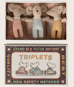 Three baby mice in checkered outfits from Maileg's "Baby Mice in Matchbox - Checker Triplets" set are snugly tucked into a vintage-style matchbox bed labeled "Triplets," which is adorned with an illustration of three baby mice driving cars.