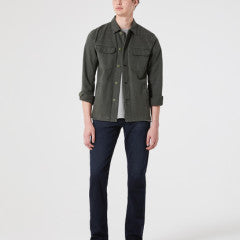 A person wears a green button-up shirt, white undershirt, and AG Jeans' Tellis Denim Bundled Jeans in a modern slim dark wash against a plain background.