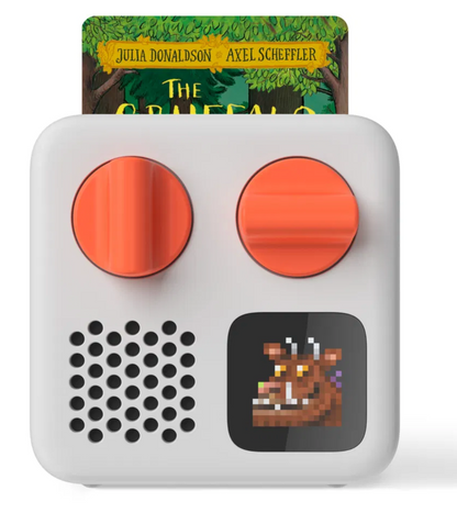 The Yoto Mini Player by Yoto is a compact, screen-free audio device equipped with two orange knobs, a speaker, and a small screen showcasing a pixelated creature. In the background, the book "The Gruffalo" can be seen, suggesting limitless storytelling experiences.