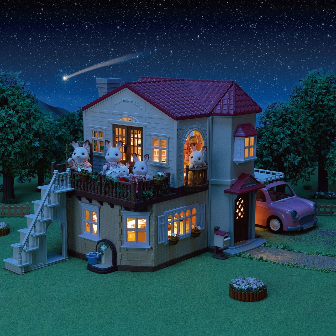 A Calico Critters animal family, featuring the cherished Chocolate Rabbit family, is gathered in and around the Country Home-Secret Attic Playroom at night, its cozy interior lights shining as a pink car is parked outside the charming home beneath a star-filled sky.