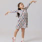A young girl in the Pink Chicken Girls' Bamboo Steph Dress and pink shoes stands on one foot, arms outstretched as if dancing, against a plain light background.