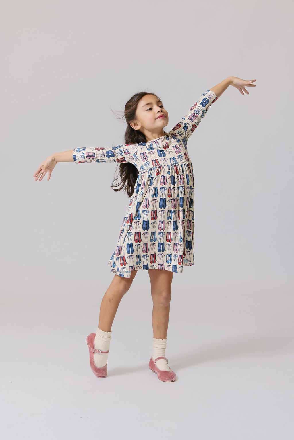 A young girl in the Pink Chicken Girls' Bamboo Steph Dress and pink shoes stands on one foot, arms outstretched as if dancing, against a plain light background.