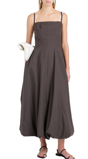 A woman models the Proenza Schouler White Label Ella Dress—an ankle-length, sleeveless fit-and-flare dark gray dress in rumpled cotton with spaghetti straps—styled with black sandals and a white clutch against a plain background.