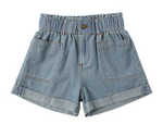 The Girls' Alba Denim Short by Rylee & Cru features light blue denim, an elastic waistband, front button and zip closure, two front patch pockets, and rolled cuffs, displayed on a white background.