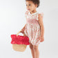 A young child wears the Kidiwi Baby Girls' Julyne Smocked Girl Romper and red shoes, holding a straw basket with red fabric trim, against a plain white background.