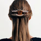 A person with long, straight brown hair is wearing two Machete Jumbo Heirloom Claws made from Italian acetate at the back of their head.